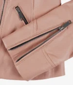 Close-up of a blush pink leather jacket showing detailed stitching and silver zippers on the pockets and sleeve, conveying a sleek, stylish look.