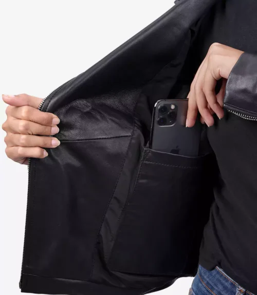 A person is placing a smartphone into an inner pocket of a black leather jacket. Their other hand holds the jacket open, revealing a smooth lining.