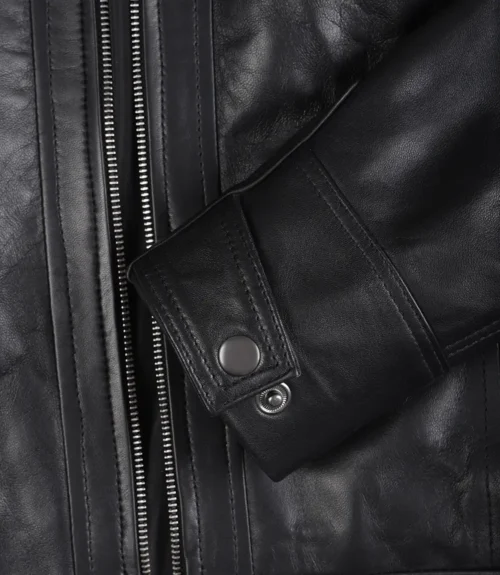 Close-up of a black leather jacket's sleeve with visible zipper and snap button detail. Texture appears smooth and polished, conveying a sleek, stylish tone.