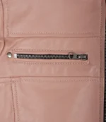 Close-up of a pink leather jacket featuring a horizontal silver zipper pocket with detailed stitching and a rivet on the upper left.
