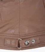 Close-up of a brown leather jacket's hem with visible stitching and a metal snap button. The texture is smooth, conveying a sleek, stylish look.