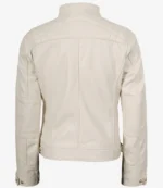 A cream-colored jacket with quilted shoulder details is shown from the back. It features buttoned cuffs, a simple collar, and a straight hemline.