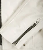 Close-up of a white leather jacket showcasing sleek stitching, a silver zipper partially open, and a metal snap button, conveying a modern, stylish look.