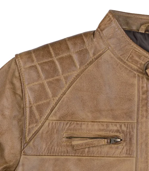 Close-up of a brown leather jacket featuring quilted shoulder detailing and a small zippered chest pocket. The leather has a rugged, textured appearance.