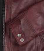 Close-up of a burgundy leather jacket sleeve with stitching detail and a silver button. The texture conveys a sense of rugged sophistication.
