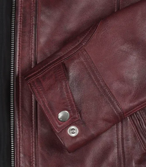 Close-up of a burgundy leather jacket sleeve with stitching detail and a silver button. The texture conveys a sense of rugged sophistication.
