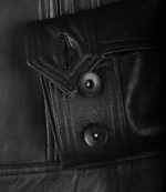 Close-up of a black leather jacket sleeve with a textured buttoned cuff. The smooth dark material and stitching convey a sense of style and durability.