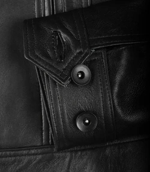 Close-up of a black leather jacket sleeve with a textured buttoned cuff. The smooth dark material and stitching convey a sense of style and durability.