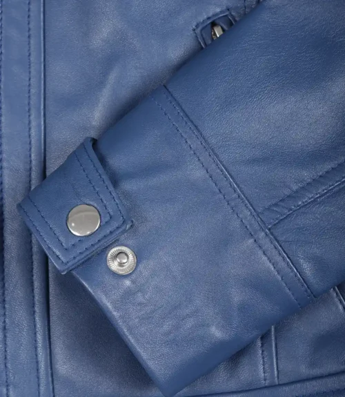Close-up of a blue leather jacket showing a sleeve with detailed stitching and shiny metal snaps. The texture is smooth, conveying a polished, modern look.