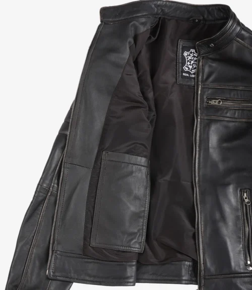 Open black leather jacket showing the interior lining. Features several pockets and visible zippers. The label reads Real Leather. Sleek, modern design.