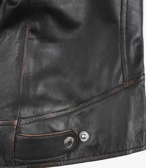 Close-up of a black leather jacket's lower section, featuring a silver snap button and a decorative strap. The leather appears smooth and slightly worn.
