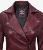 Close-up of a maroon leather jacket with a notched collar and silver snaps. The inner label displays a design logo. The leather appears sleek and polished.