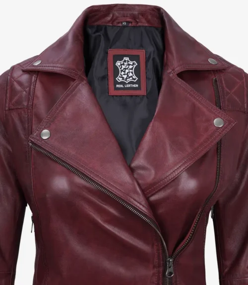 Close-up of a maroon leather jacket with a notched collar and silver snaps. The inner label displays a design logo. The leather appears sleek and polished.