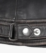 Close-up of a dark brown leather jacket detail showing a belt strap with a shiny silver buckle and snap button. The leather texture is visibly worn.