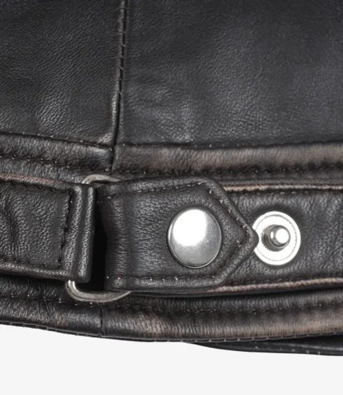 Close-up of a dark brown leather jacket detail showing a belt strap with a shiny silver buckle and snap button. The leather texture is visibly worn.