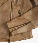 Close-up of a brown leather jacket showing detailed stitching, zippers, and a folded sleeve. Texture is smooth and slightly worn, giving a rugged feel.