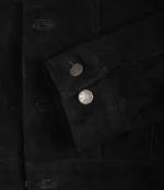 Close-up of a black suede jacket shows detailed stitching and two metallic buttons on a folded sleeve, conveying a sleek and stylish look.