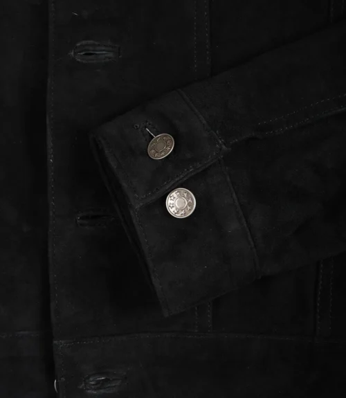 Close-up of a black suede jacket shows detailed stitching and two metallic buttons on a folded sleeve, conveying a sleek and stylish look.