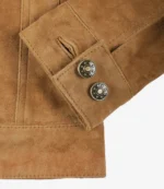 Close-up of a tan suede jacket's cuff with two brass snap buttons featuring a star design. The texture conveys a rustic and stylish elegance.