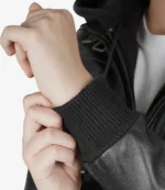 Close-up of a person adjusting the cuff of a black leather jacket. The focus is on the textured, ribbed knit cuff, conveying a sense of style and sophistication.